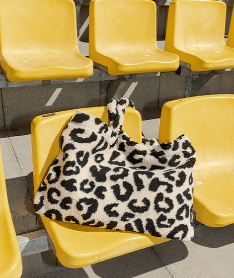 Eine große Leoprint-Tasche liegt auf einem gelben Sitz einer Stadiontribüne; Zu Taschen Damen gehen